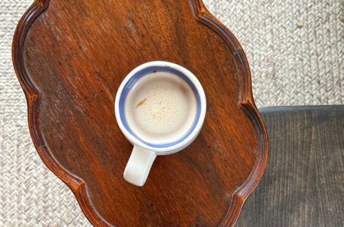 cup of coffee sitting on a scalloped edged wood drink table next to a wood bench