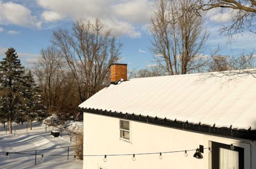 carriage house with white paint, black metal roof, and black door covered in snow.