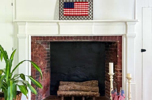 woven american flag on an antique grate made with yarn. It sits above a large fireplace in a colonial era home