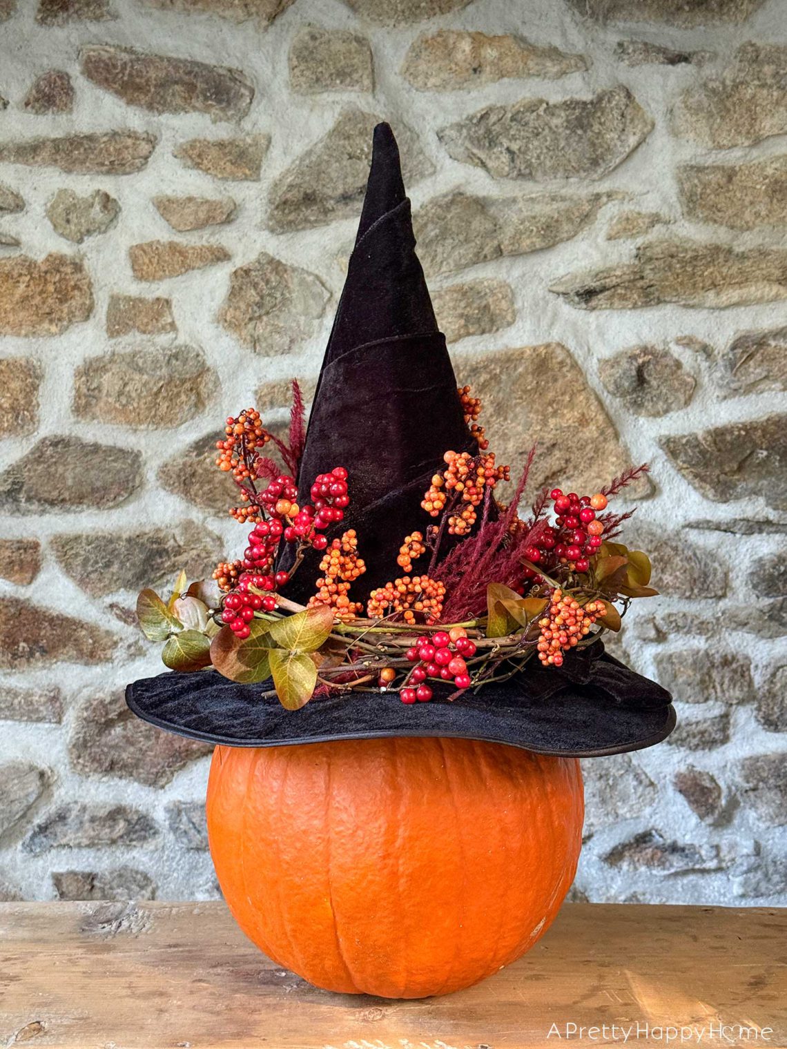 diy floral witch's hat sitting on a pumpkin in front of a stone wall