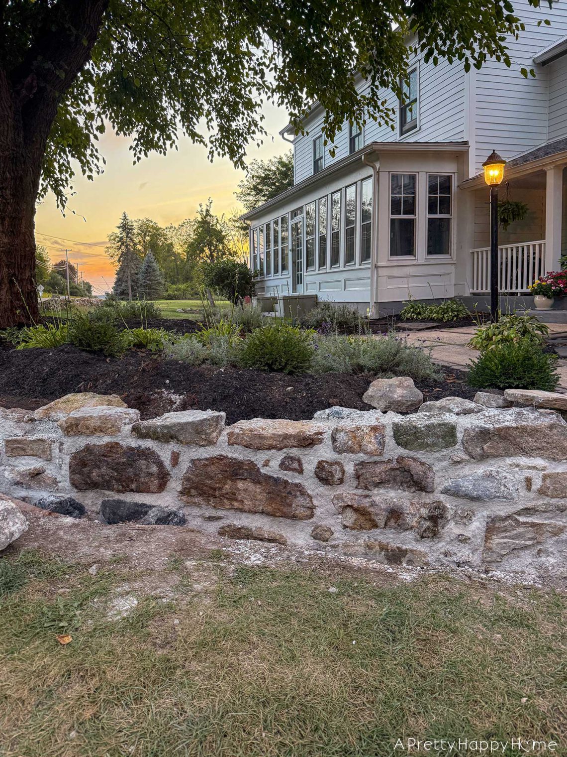 Curved Fieldstone Wall under construction using historical masonry technique and lime mortar in front of an old farmhouse