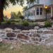 Curved Fieldstone Wall under construction using historical masonry technique and lime mortar in front of an old farmhouse