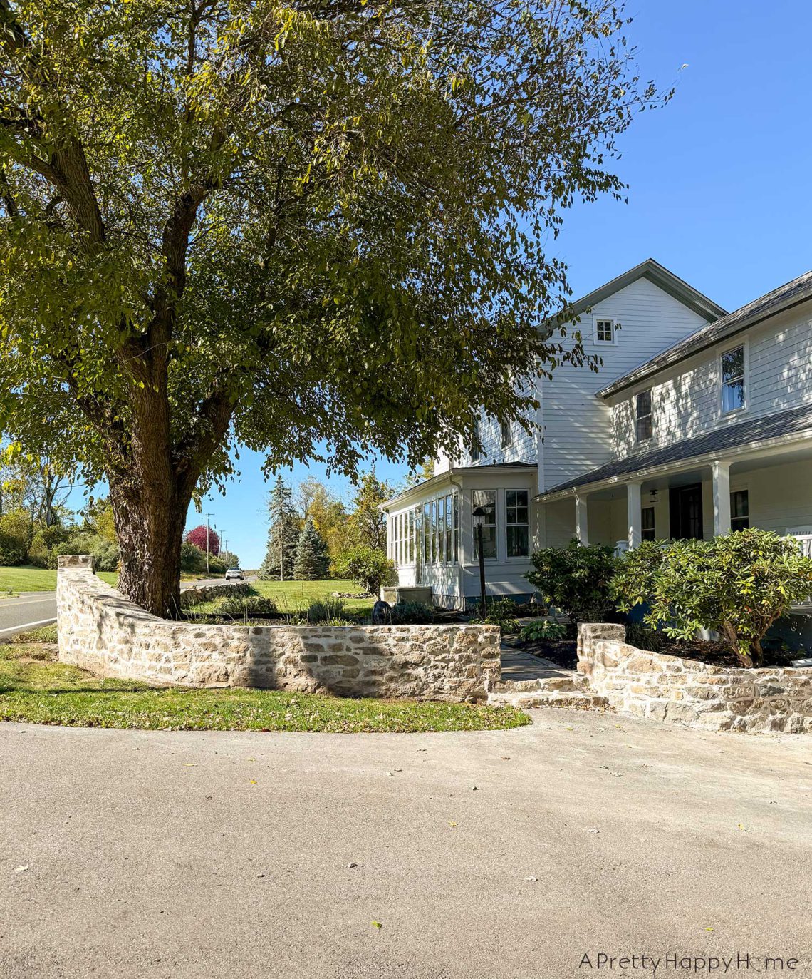 colonial farmhouse from the 1780s painted white standing behind a curved fieldstone wall