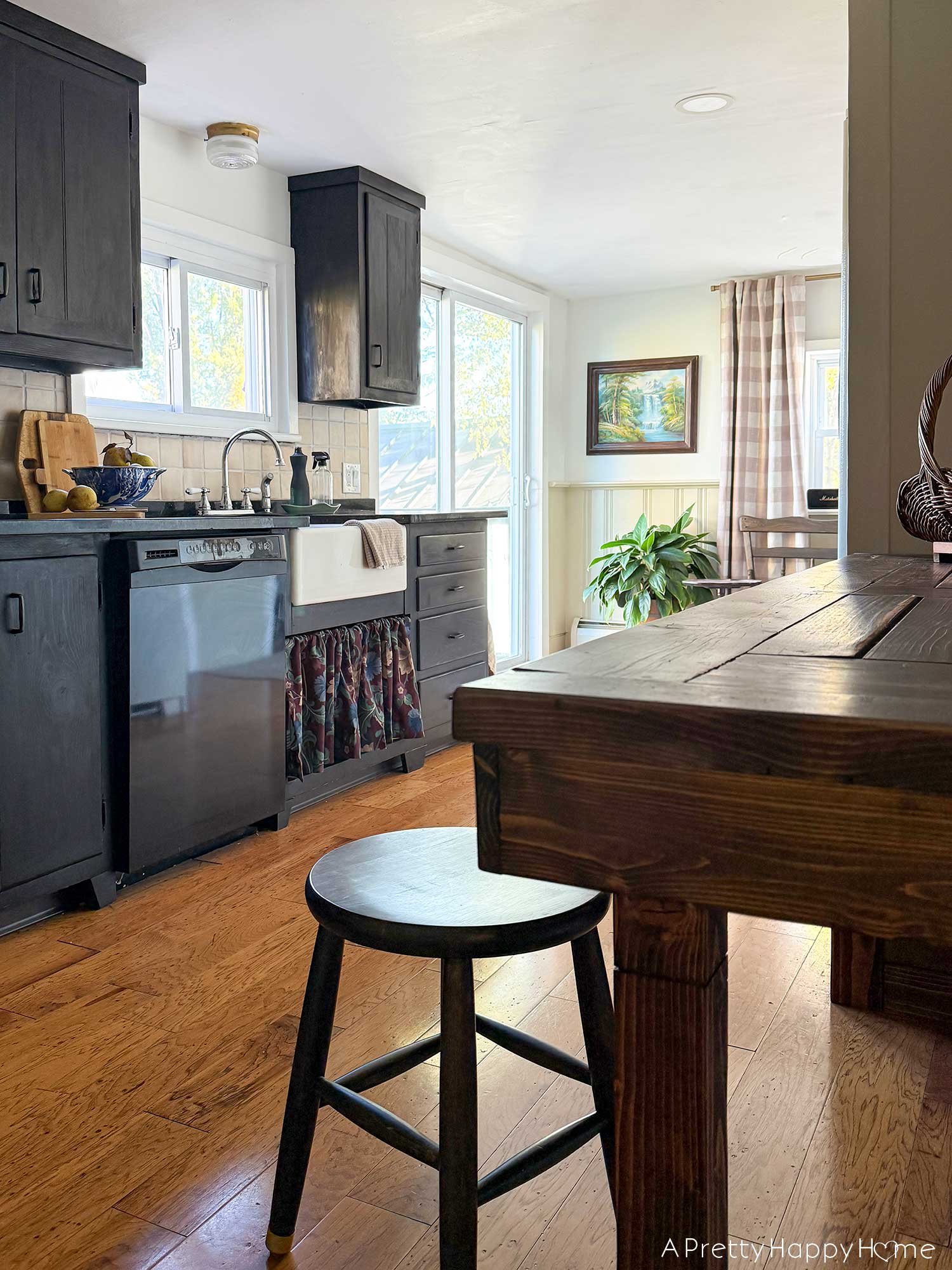 dark cottagecore kitchen with black cabinets, wainscoting, and a table as a work surface.