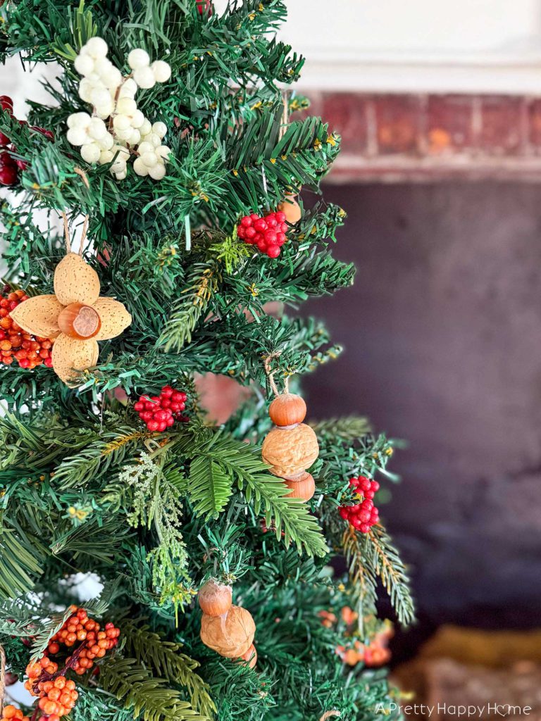 christmas tree showing detail of ornaments made by hot glueing in-shell nuts together. Four almonds and one hazelnut can be hot glued together to make a flower. Two hazelnuts and a walnut can be glued together in a vertical stack. The handmade nut ornaments are hung by glueing a looped string to the back of the ornament. On the blog post five ways to decorate with nuts for christmas. 