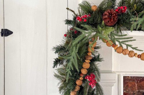 christmas garland with greenery and it is wrapped with a handmade nut garland of in-shell walnuts, almonds, and hazelnuts. the garland is draped over a white fireplace with brick surround and is featured on the blog post five ways to decorate with nuts for christmas