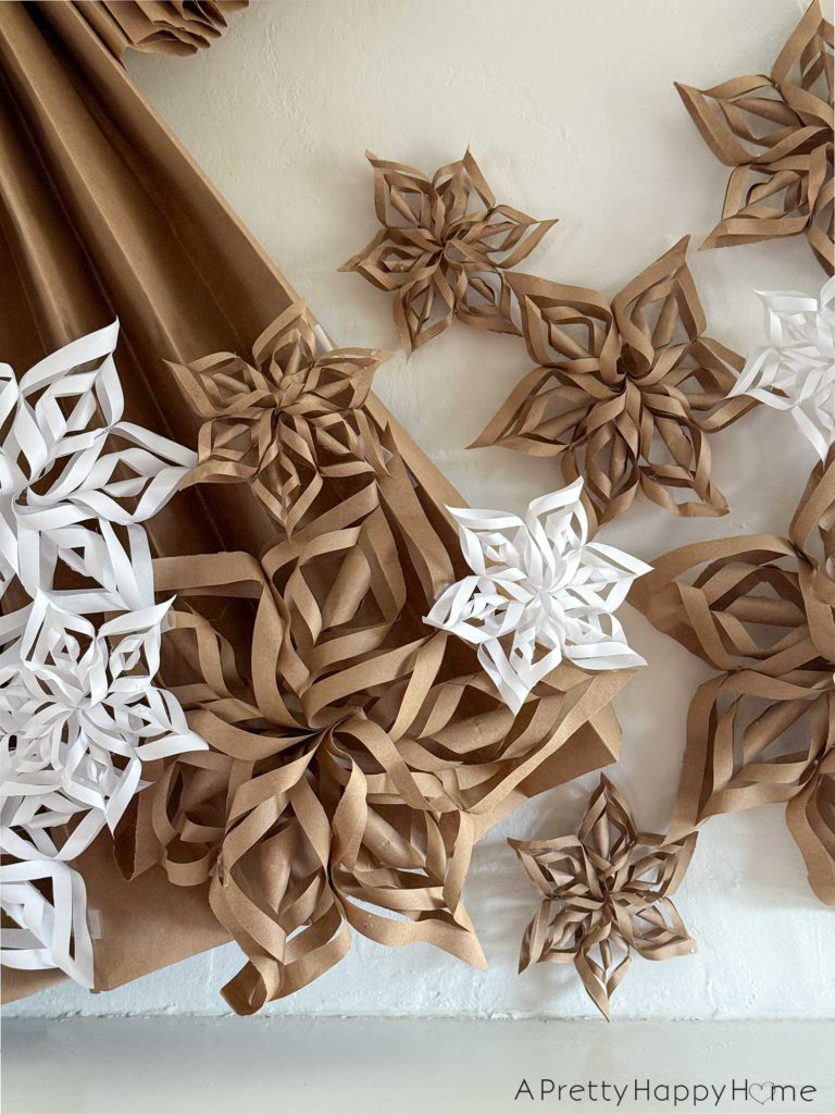 paper snowflakes of varying sizes made from white computer paper and brown kraft paper taped to an overmantel, the spot above a fireplace mantel, to decorate a giant paper angel.