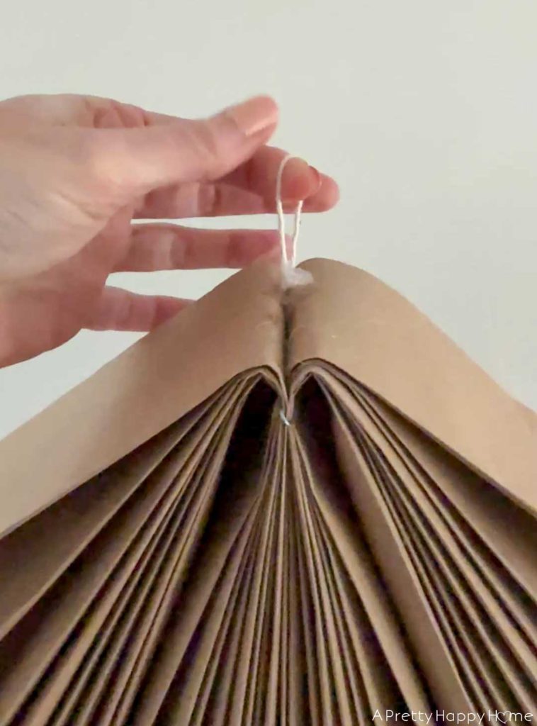 how to make a giant paper angel out of kraft paper. image shows a hanging loop made from twine hot glued in between two halve of the folded paper angel