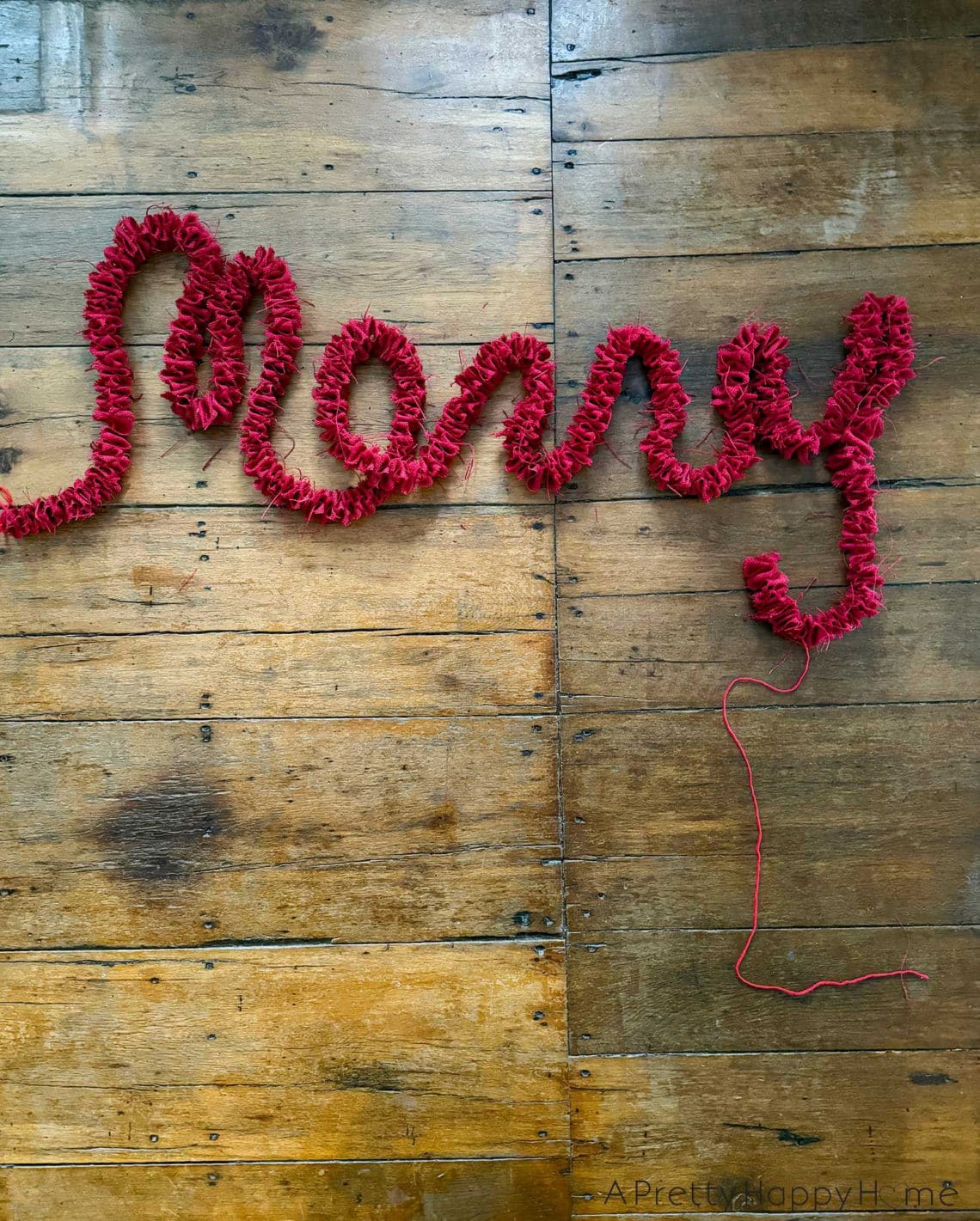 red burlap garland arranged in the shape of the word merry set against the background of rustic wood flooring