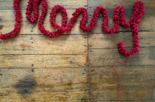 red burlap garland arranged in the shape of the word merry set against the background of rustic wood flooring