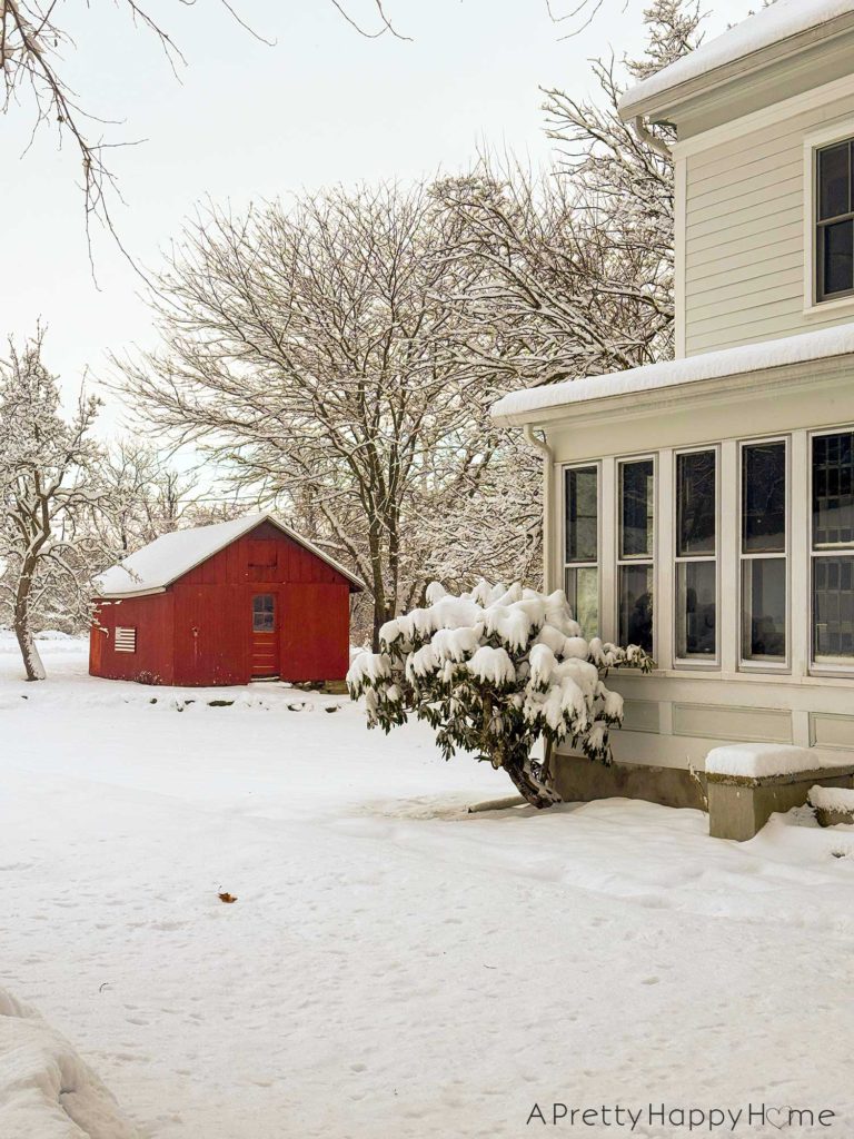 picture of a white farmhouse covered in snow. there is a small red barn in the background.