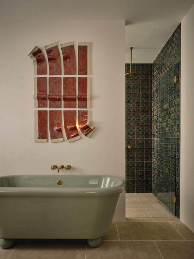 bathroom designed by jase sullivan and featured on desire to inspire that shows a large mint green soaking tub with round feet. There's a brown and white wall sculpture on the wall behind the tub. A doorway opens into a walkin shower tiled with green tiles.