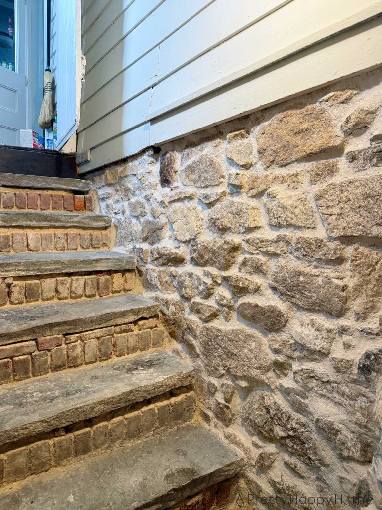 flagstone stairs to a basement with brick risers. the sides of the stairwell are fieldstone. The brick risers have been chipped out of old lime mortar in preparation for new lime mortar to be installed.