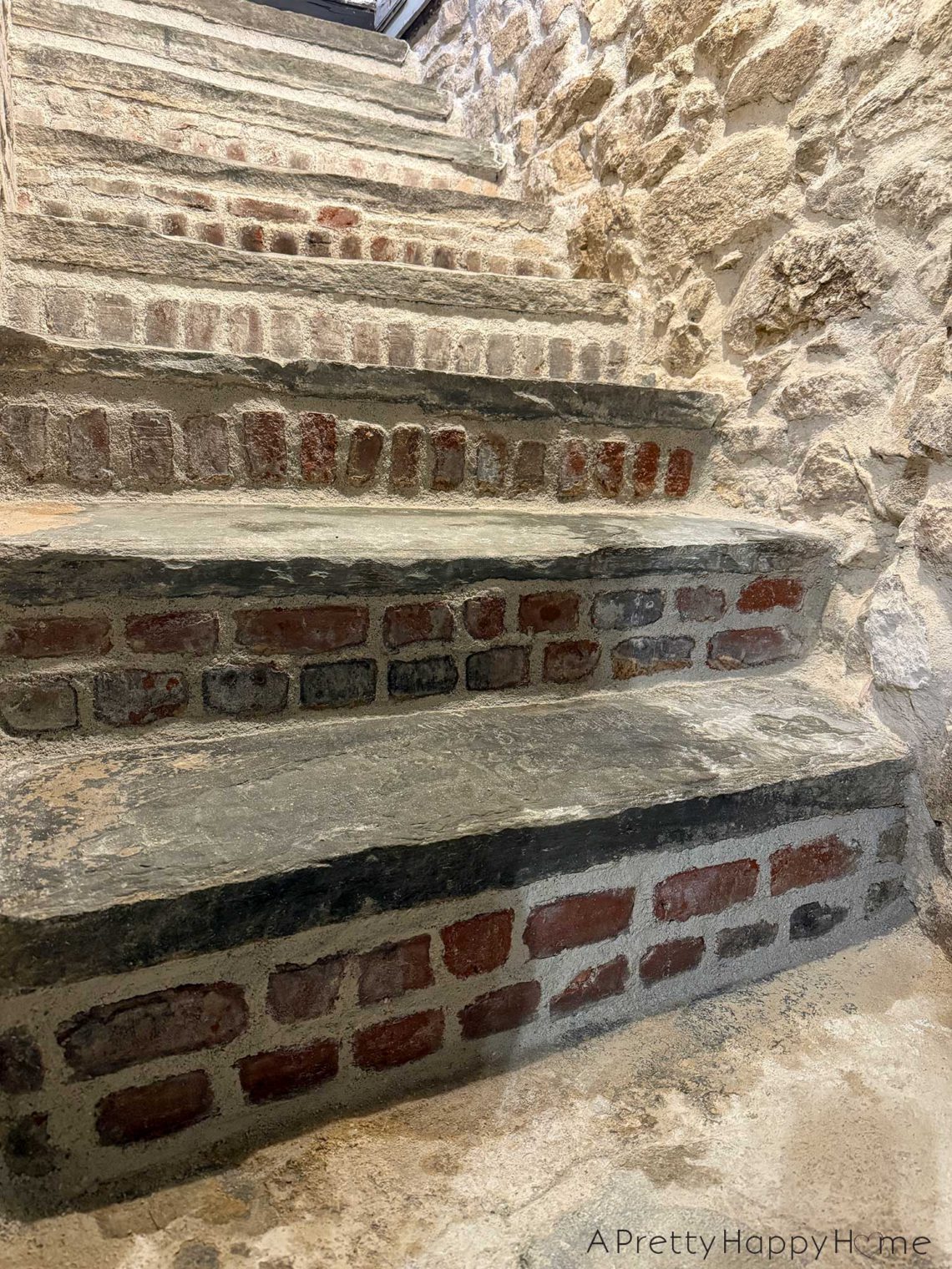 flagstone stairs to a basement with brick stair risers. the walls of the stairwell on fieldstone.