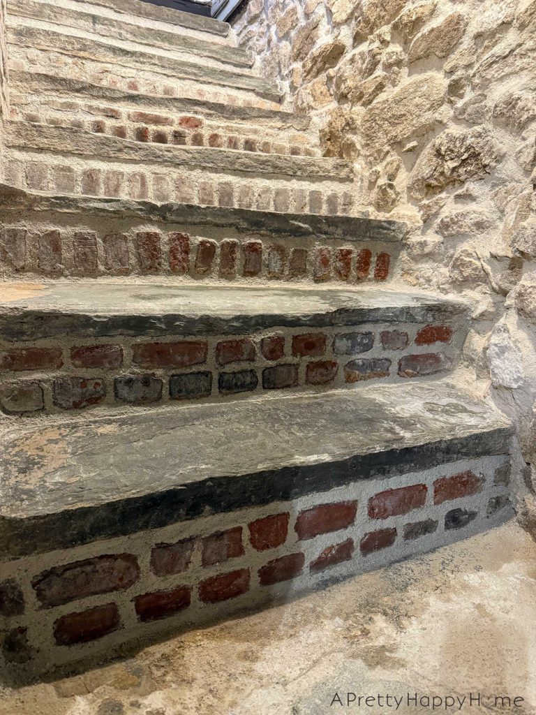 flagstone stairs to a basement with brick stair risers. the walls of the stairwell on fieldstone.