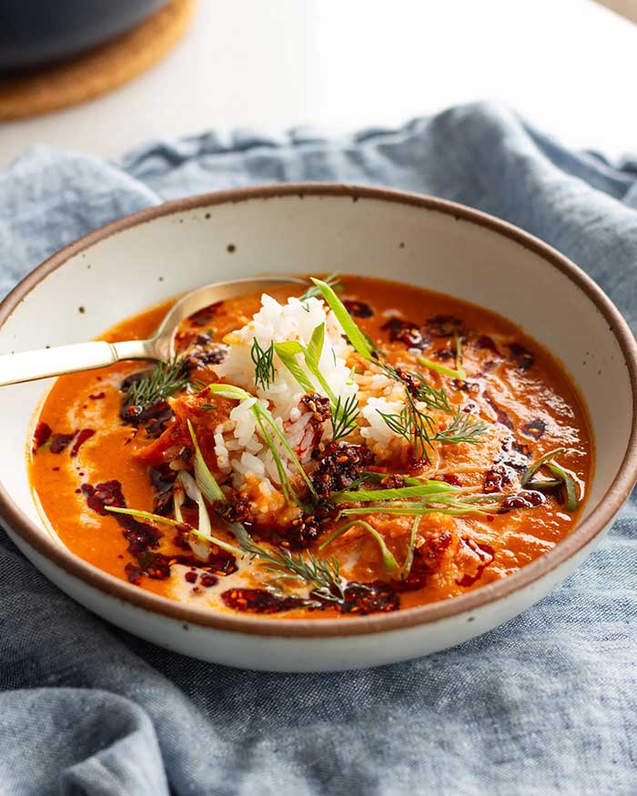 photo of justine doiron's caramelized gochujang tomato soup. It's a bowl of tomato soup topped with a drizzle of chili crisp, a mound of white rice, and green onions. Shown on the Happy List.