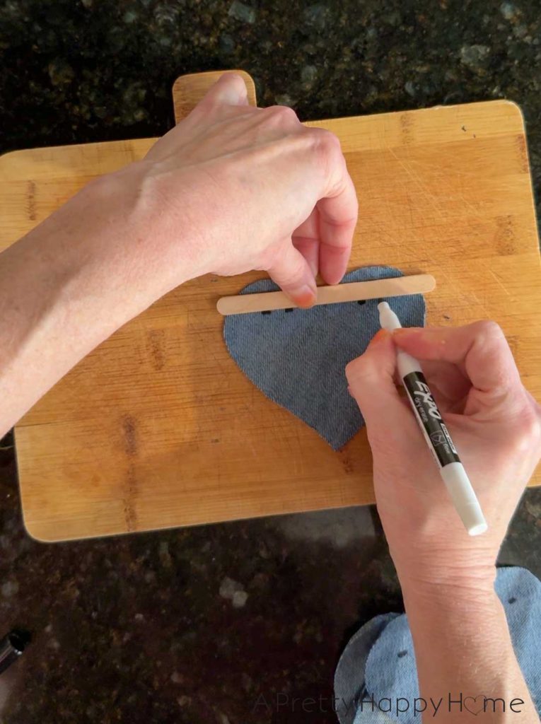 two hands marking lines on the back of a denim heart with a marker and a straight edge to know where to cut to hang the denim heart on a banner or bunting line