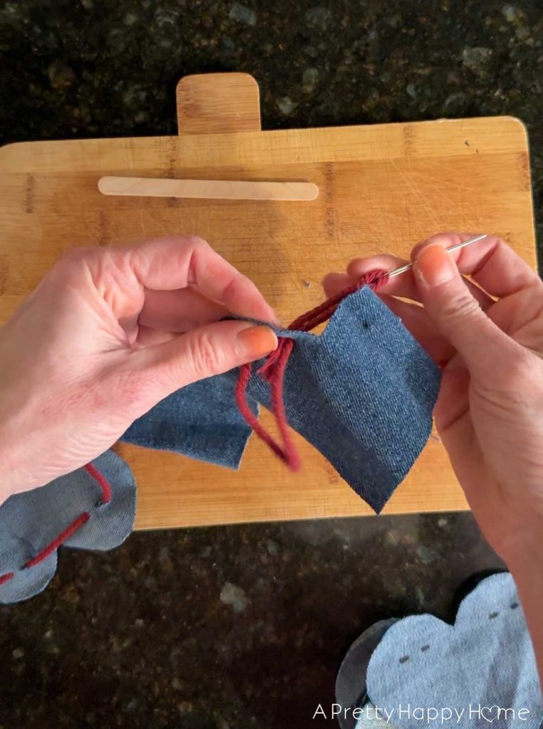 two hands threading a denim heart onto a red macrame cord to make a heart bunting
