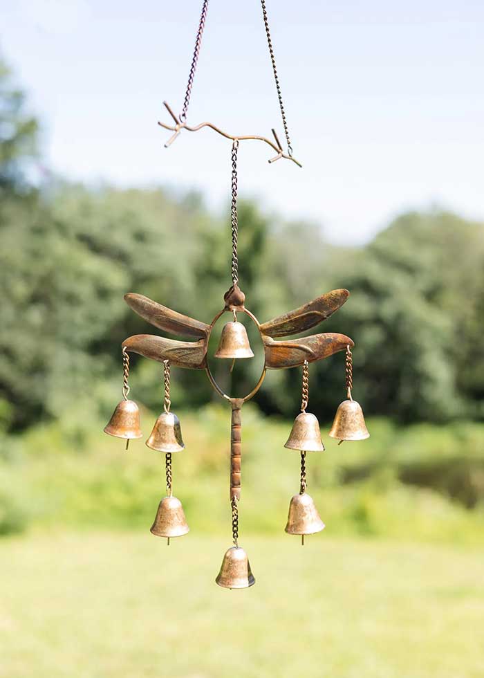 a metal dragonfly wind chime hanging from a metal branch with 7 metal bells that make the chime. Made by Etsy shop HappyGardensArt shown on the Happy List.