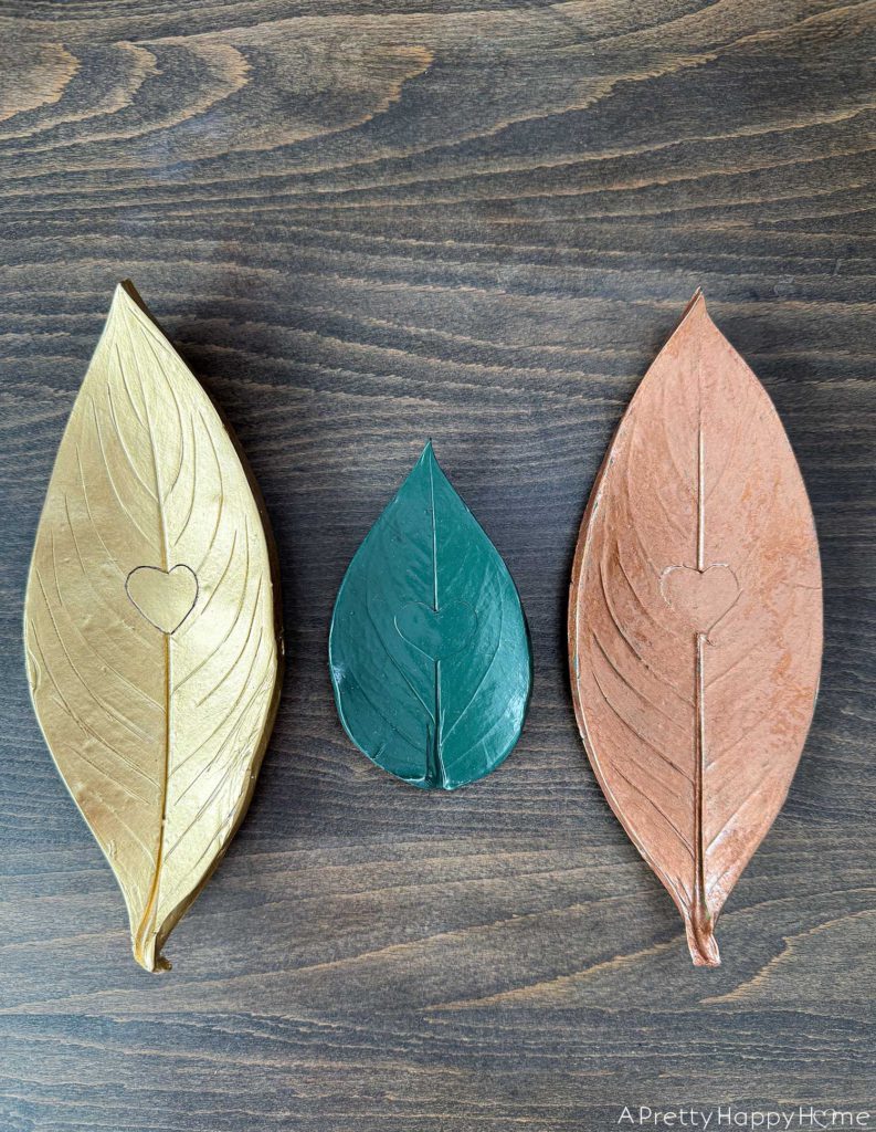 three polymer clay oven bake leaf trinket dishes in a row. One is gold, a smaller one is green, the third one is copper.
