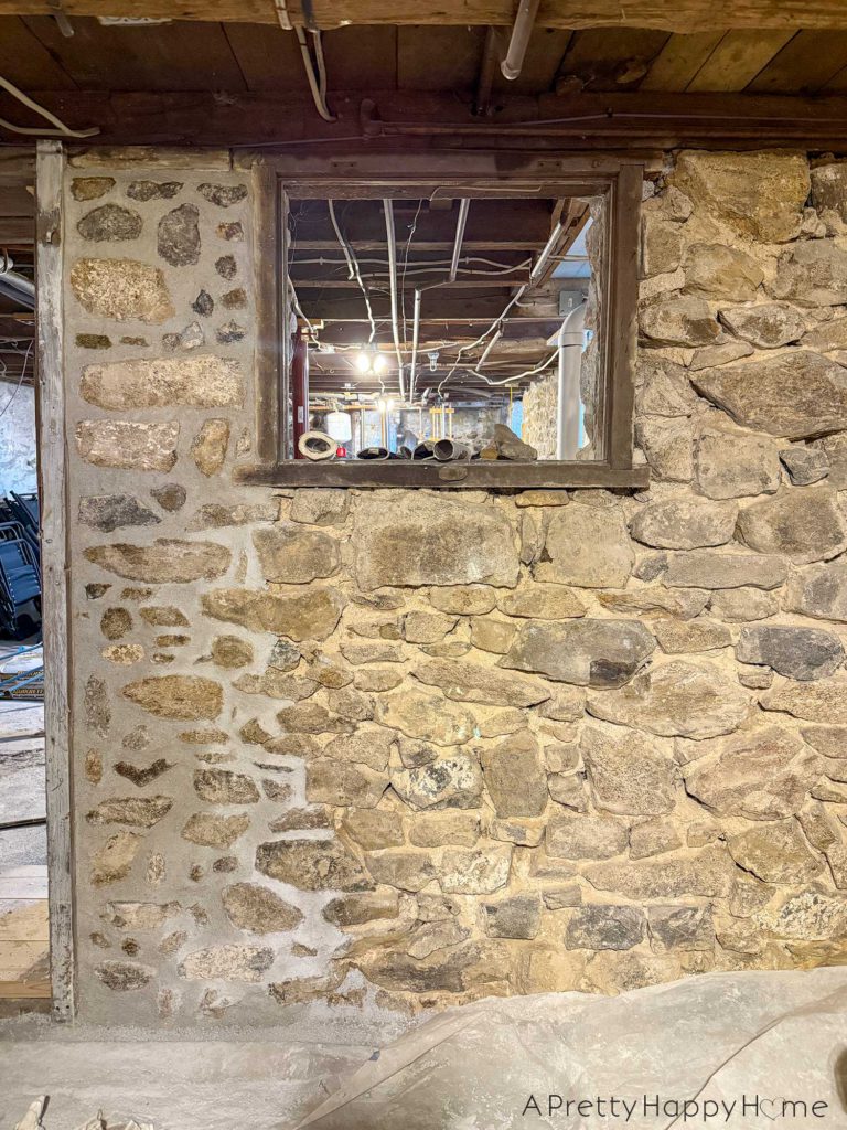 picture of a basement workshop stone repointing project showing a stone foundation wall that needs to be repointed with new lime mortar. The wall has been chipped out, meaning the old outer layer of mortar has been removed. One section has been repointed with new lime mortar.