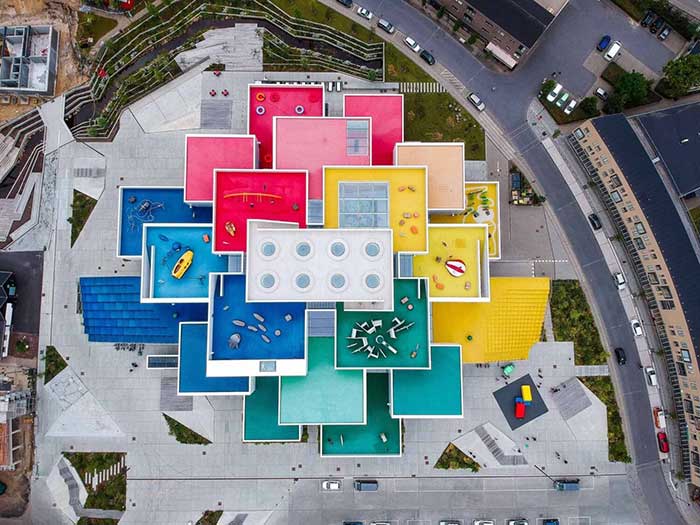 drone photo of the colorful rooftop terraces of lego house in denmark. They are red pink, yellow, blue, green, and white and feature playgrounds on the roof.