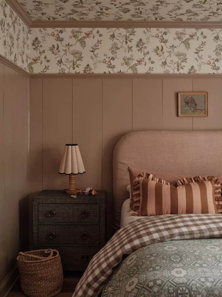pink bedroom with wallpaper above the wainscoting that extends to the ceiling. Pink theme continues with the headboard and bedding.
