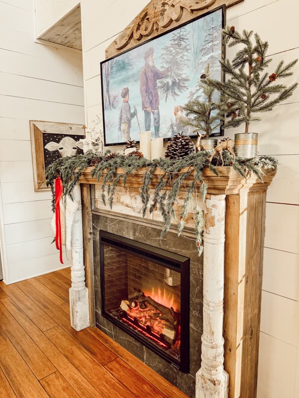 farmhouse style fireplace with mantel decorated for christmas. TV hangs above mantel showing artwork using the youtube app so you don't have to buy a frame tv. idea from the ponds farmhouse