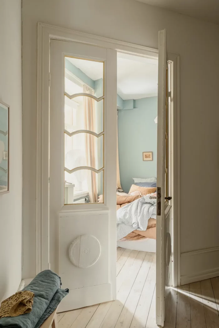 turn of the century scandinavian apartment featured on the nordroom that shows french doors with unique half light windows opening into a blue bedroom