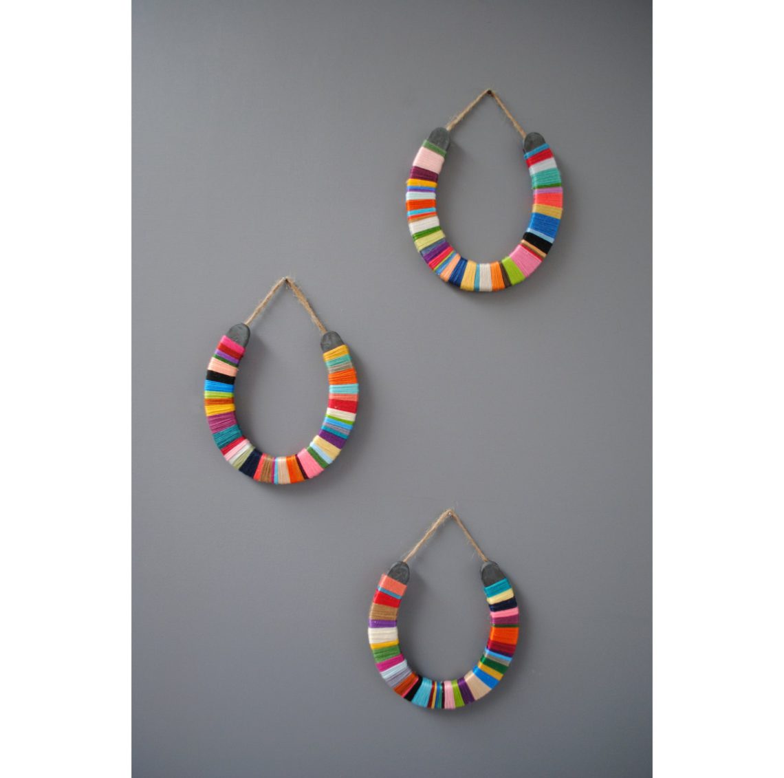 3 horses hanging on a grey background that are wrapped with colorful thread