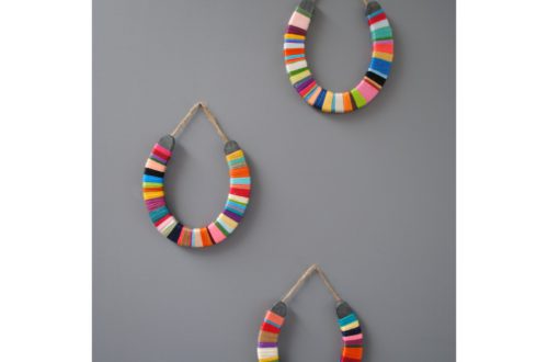 3 horses hanging on a grey background that are wrapped with colorful thread