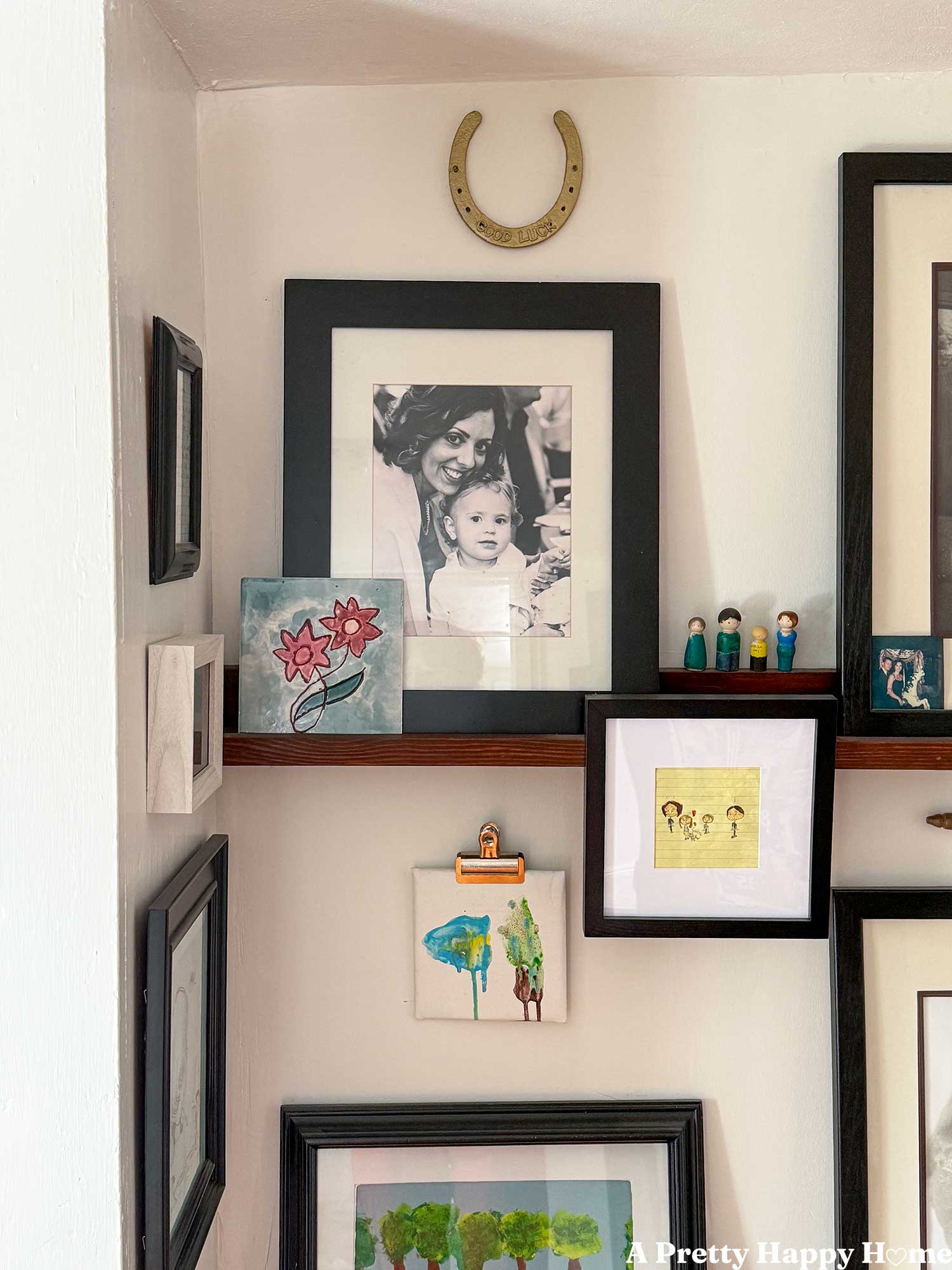 diy gold good luck horseshoe made with a horseshoe painted gold and puffy letters glued on the horseshoe to spell good luck. Horseshoe hangs on a gallery wall of family photos and mementos.