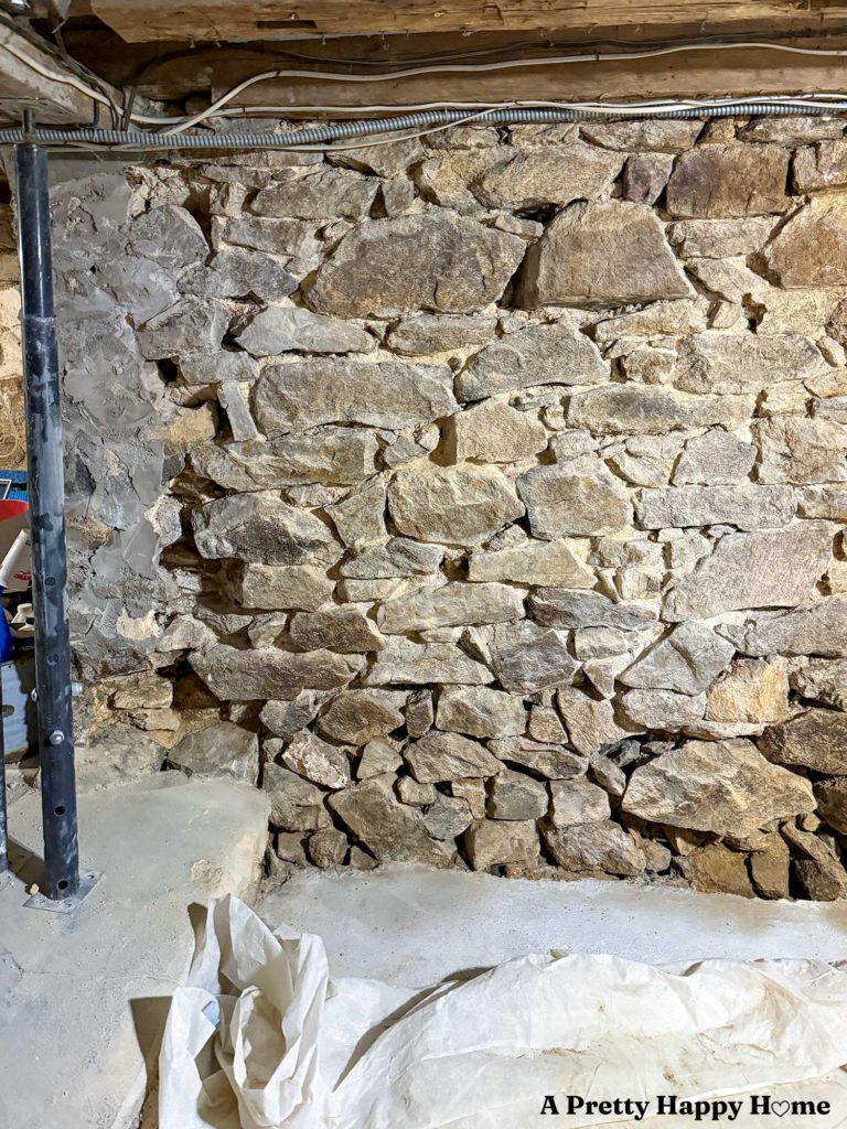 Stone foundation wall in a basement of a 1780s home that has been chipped out and ready for repointing except for a section that has concrete on it