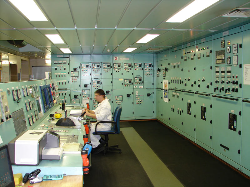 sailor in white clothes sitting at a desk in a seafood green engine control room on an oil tanker
