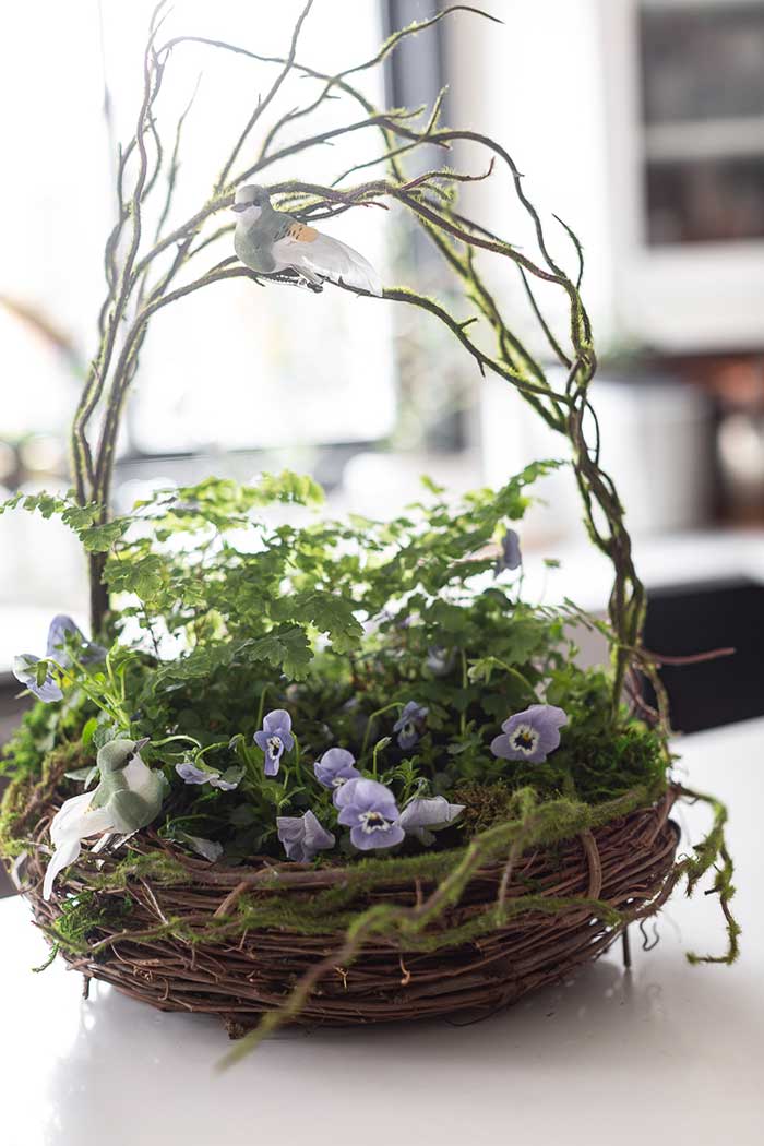 planter that looks like a nest made from two grapevines wreaths stacked together and filled with fresh plants, flowers, and faux birds for whimsy