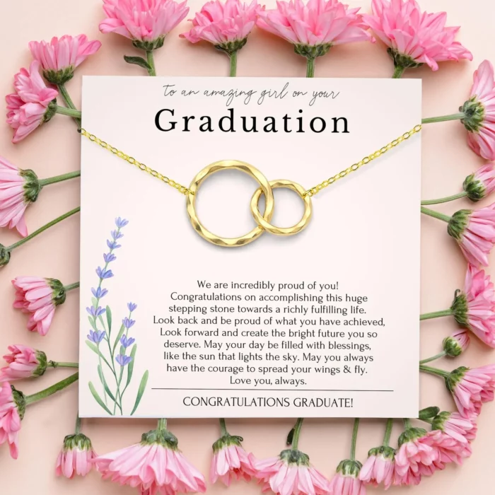 gold graduation necklace featuring two interlocking circles on a cardboard backing that has a kind graduation wish