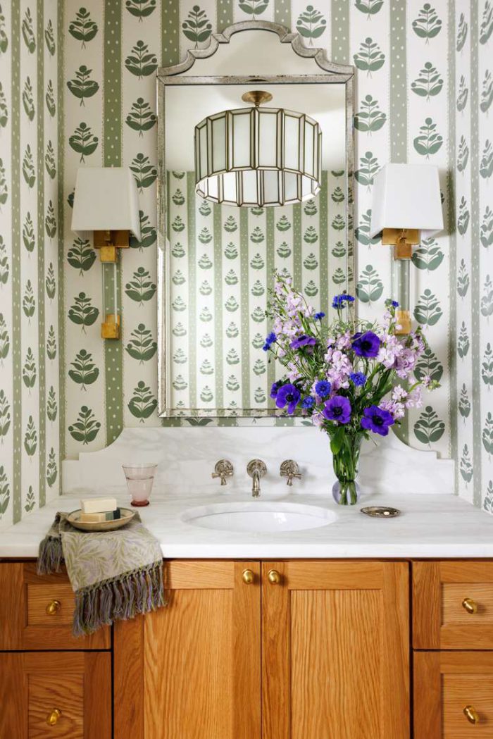 powder room with green and white wallpaper, silver-framed ornate mirror, white sconces, white countertop, and orange-toned cabinets via Martha Stewart. Photo by Mary Margaret Smith.
