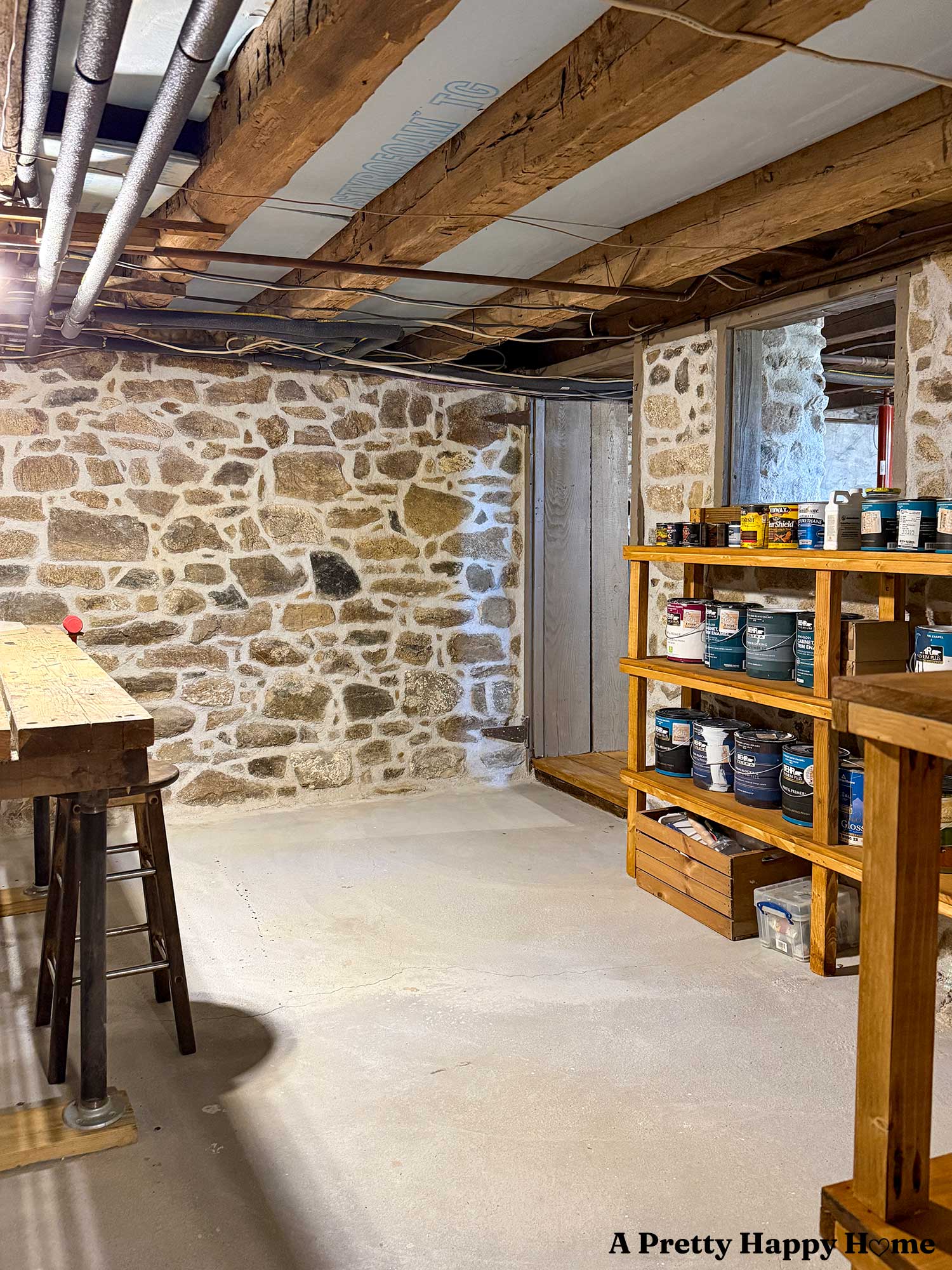 Newly repointed basement with stone walls using NHL3.5. There is a workshop area in this space with wood shelves holding cans of paint and a wood work table.