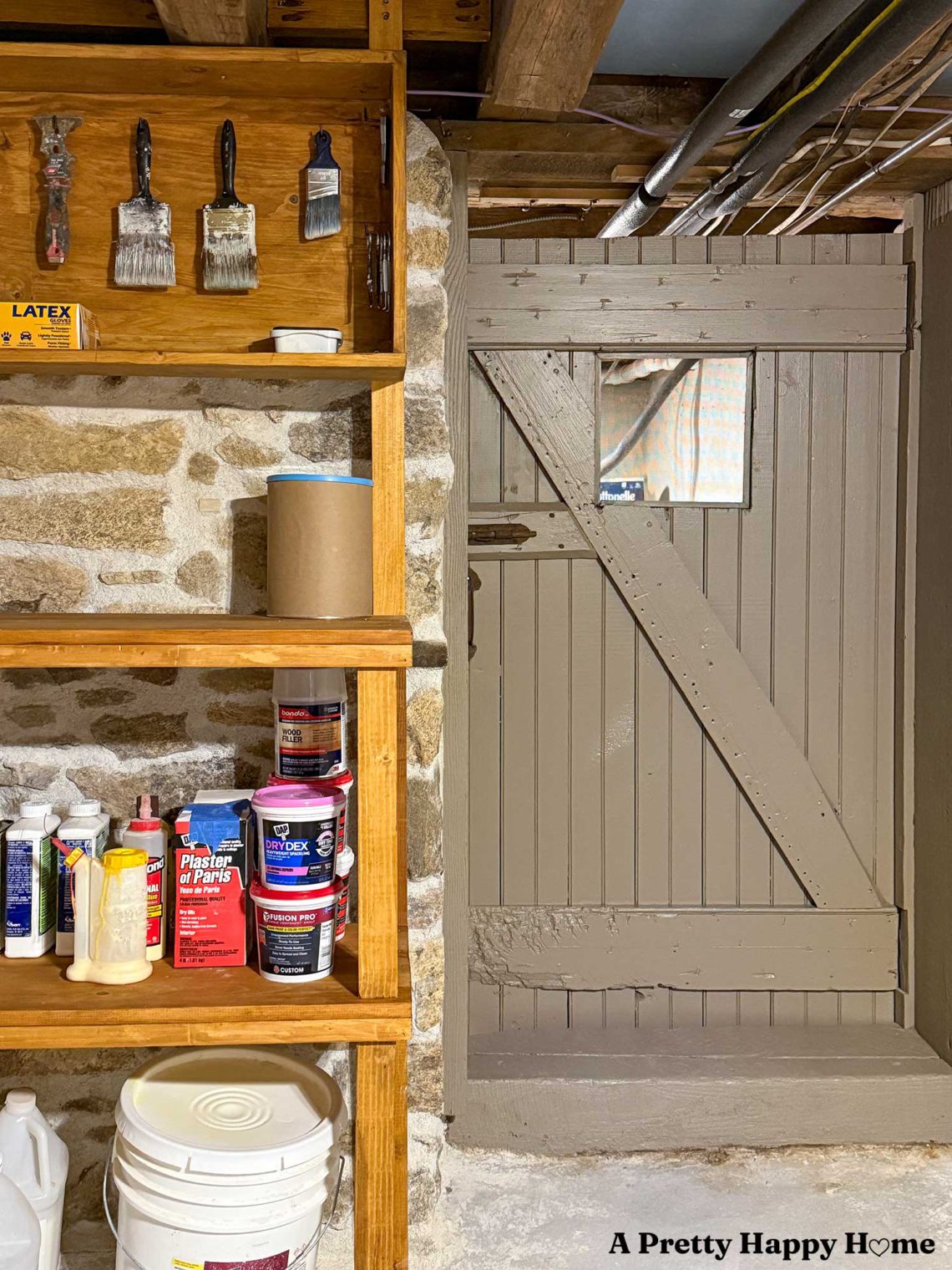 basement with stone foundation walls in a 1780s house that has been turned into a workshop with wood shelves next to a wood door painted a warm grey