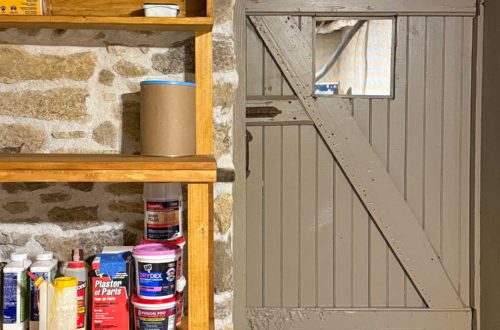 basement with stone foundation walls in a 1780s house that has been turned into a workshop with wood shelves next to a wood door painted a warm grey