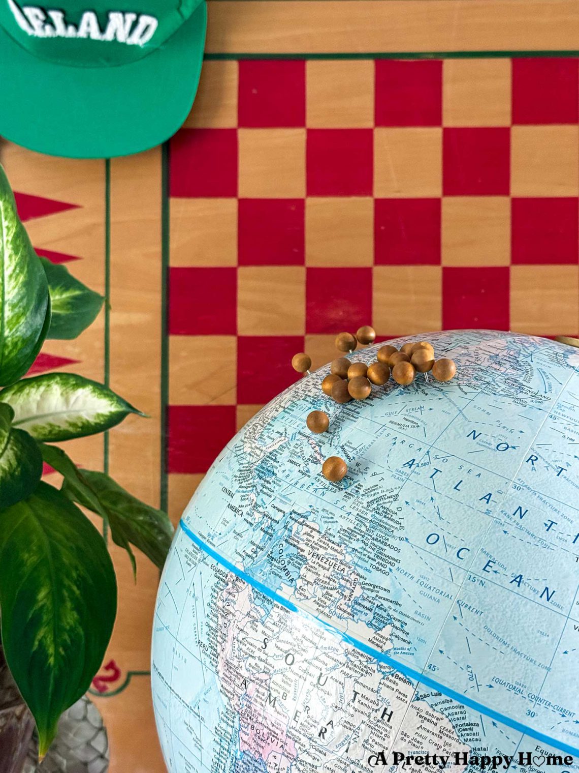 close up of a vintage globe upcyled into a diy push pin travel globe. The globe has wood push pins marking places traveled and sits in front of a checkbaord background.