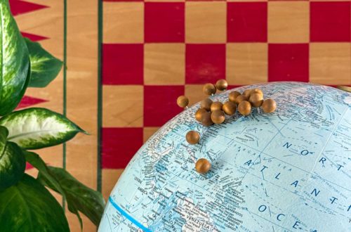 close up of a vintage globe upcyled into a diy push pin travel globe. The globe has wood push pins marking places traveled and sits in front of a checkbaord background.