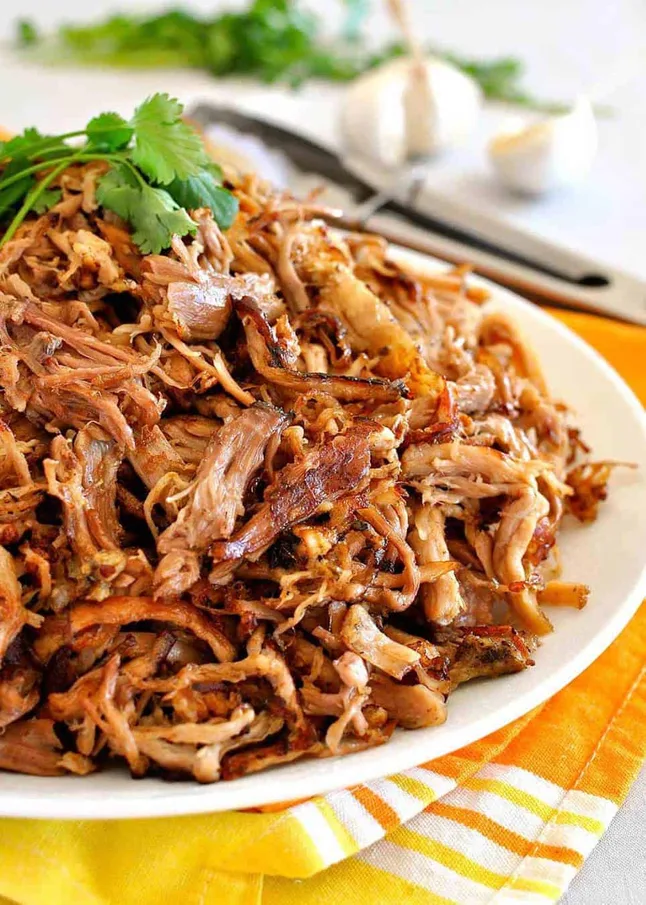 plate heaping with shredded pork carnitas with a cilantro garnish on top. Recipe from Recipe Tin Eats.