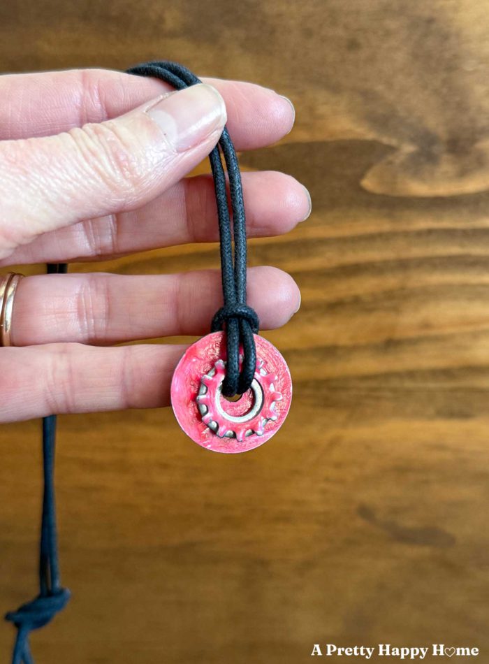 woman holding a necklace made by a child from three washers layered together. Two of them are painted pink with nail polish. They hang from a leather cord.