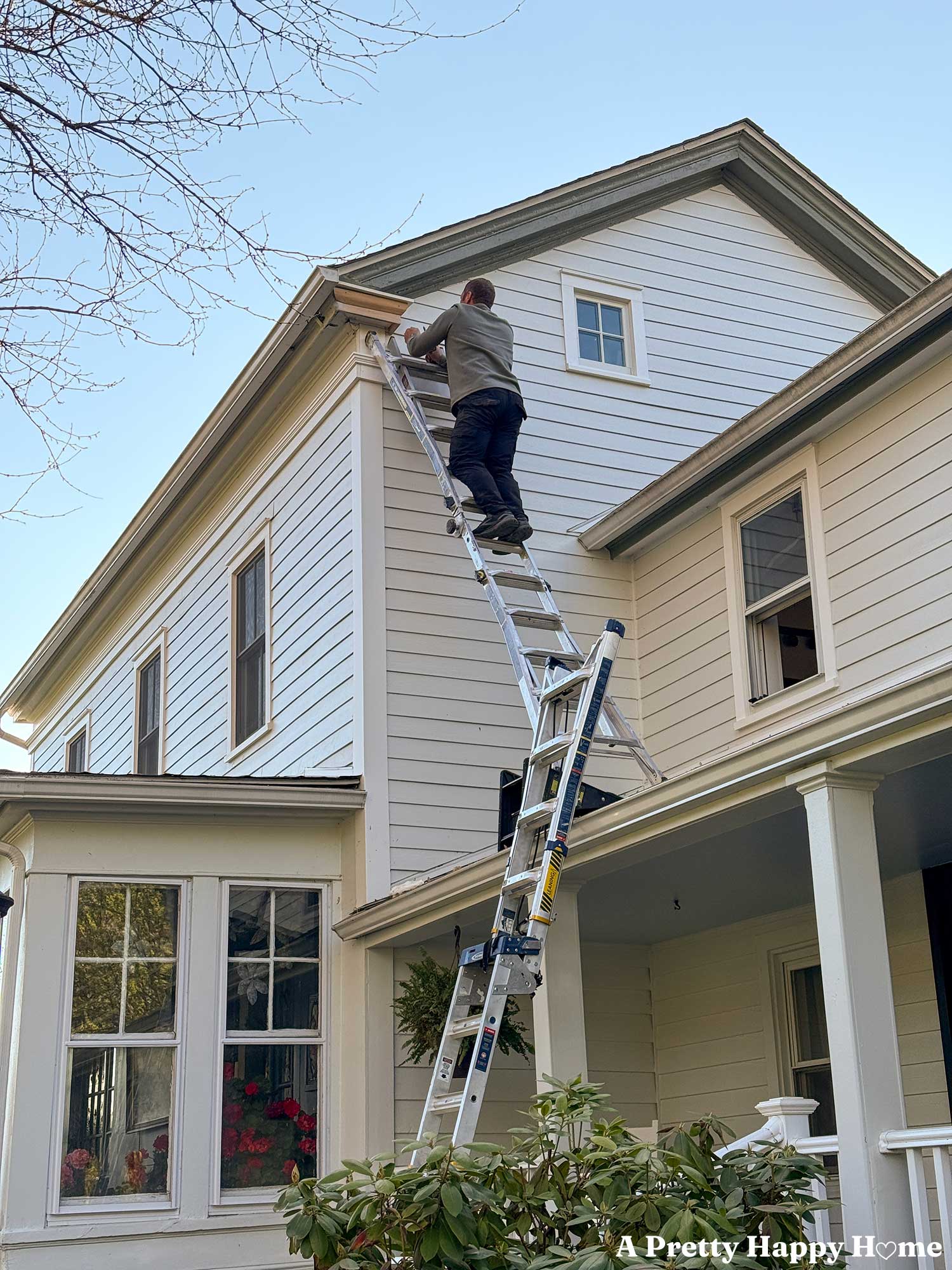 man on a ladder repairing a gable return on a greek revival style home painted white. The new trim on the gable return is made of cedar.