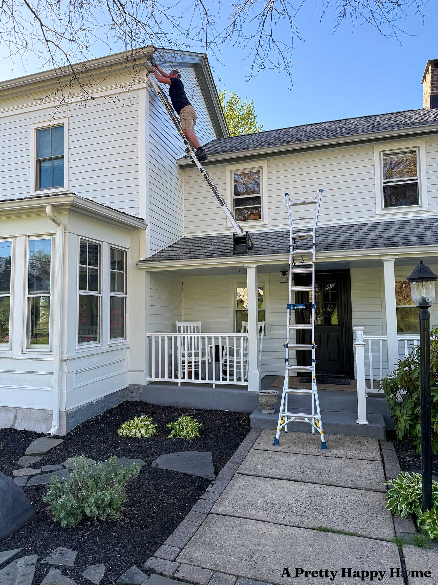 man on a ladder trying to fix a gable return on a greek revival style home that is painted white