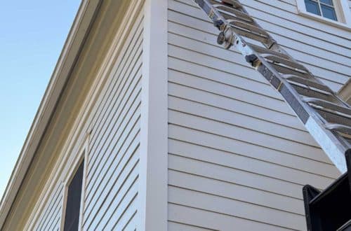 ladder going up to the roof line of a white house. There's a missing gable return on this greek revival style house that has to be rebuilt.