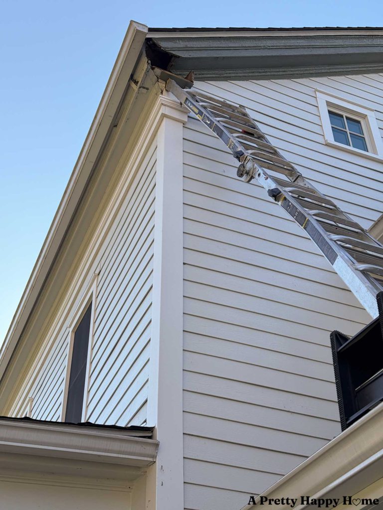 ladder going up to the roof line of a white house. There's a missing gable return on this greek revival style house that has to be rebuilt.