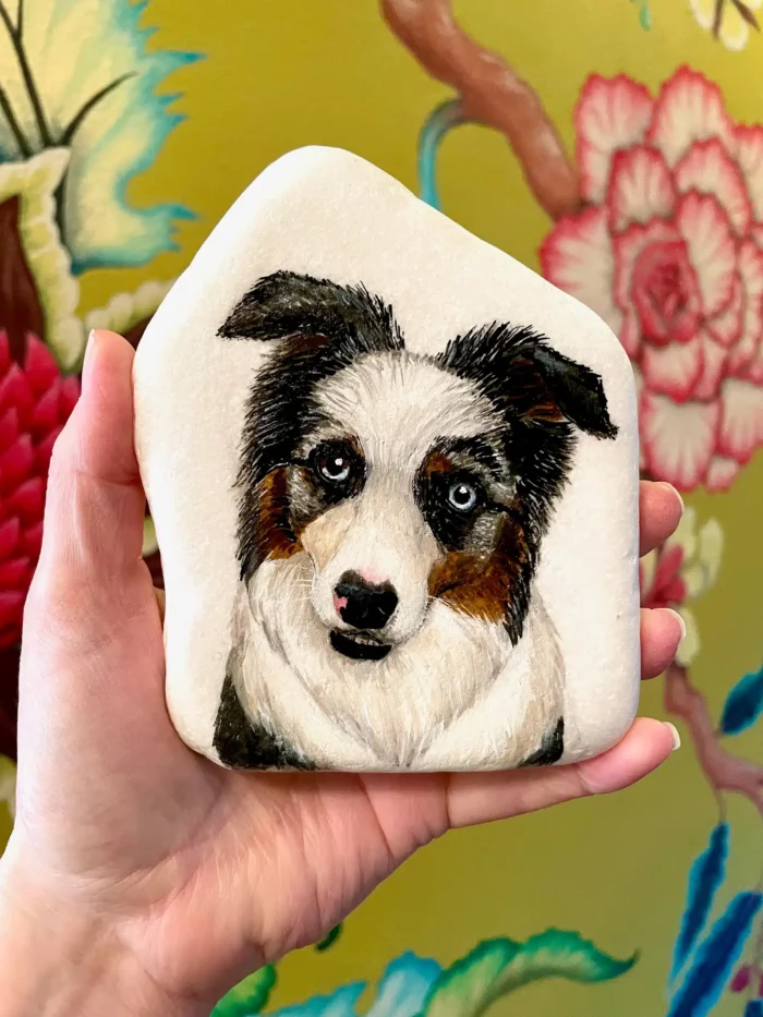 custom portrait of a dog painted on a stone and being held in someone's hand