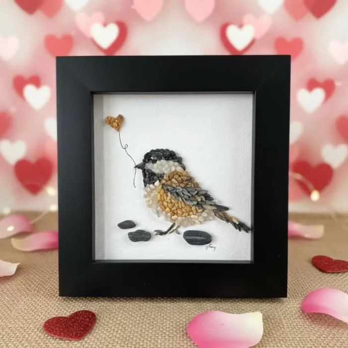 bird make out of pebbles and put into a black frame in front of a heart background
